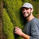 Portrait of a young man, David, working on a large moss mural, smiling.