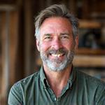 Portrait of Caleb Thorne, a rugged, experienced craftsman with a warm smile, specializing in wood and stone integration.