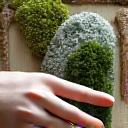 A designer's hand pointing at a tablet displaying a 3D rendering of a moss wall in a room, with material swatches laid out nearby.