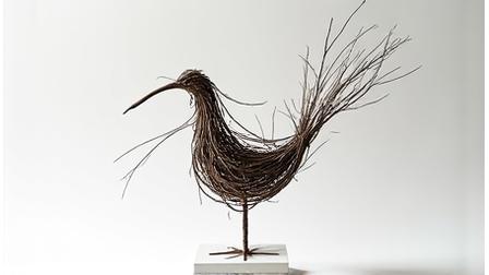 Small, abstract bird sculpture elegantly crafted from interlaced twigs, showcased on a minimalistic stand.